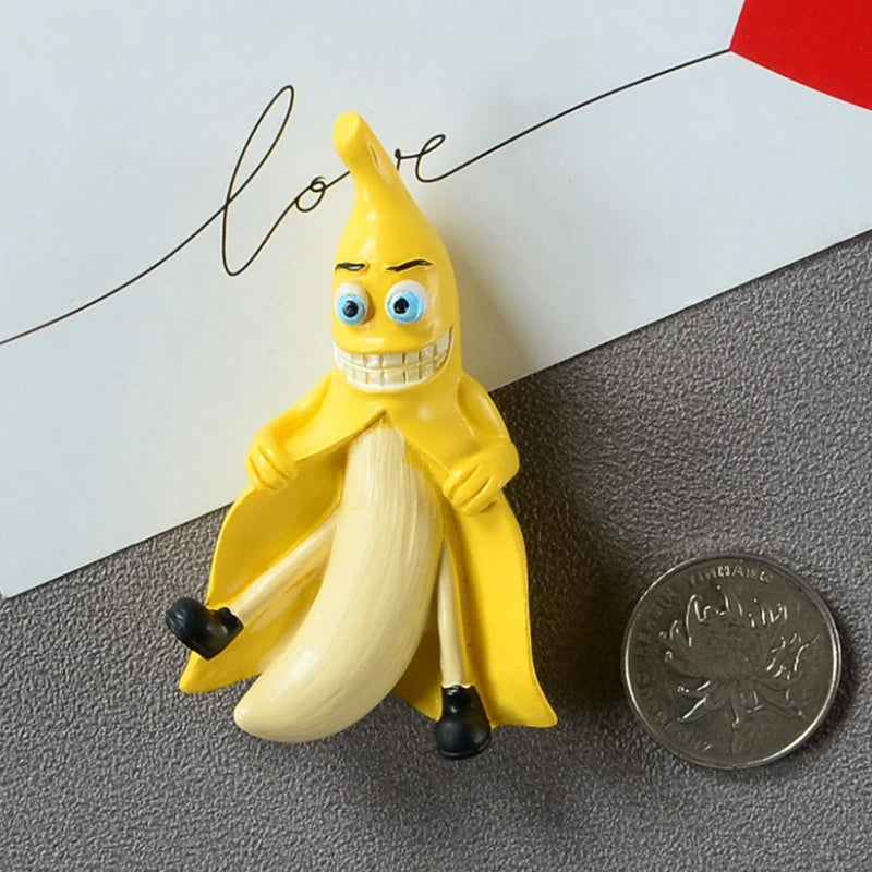 A yellow banana shaped fridge magnet with a smiling face and black accents, placed on a gray surface.