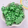 A collection of small, green resin flatback cabochon figurines with spooky faces in a white dish.