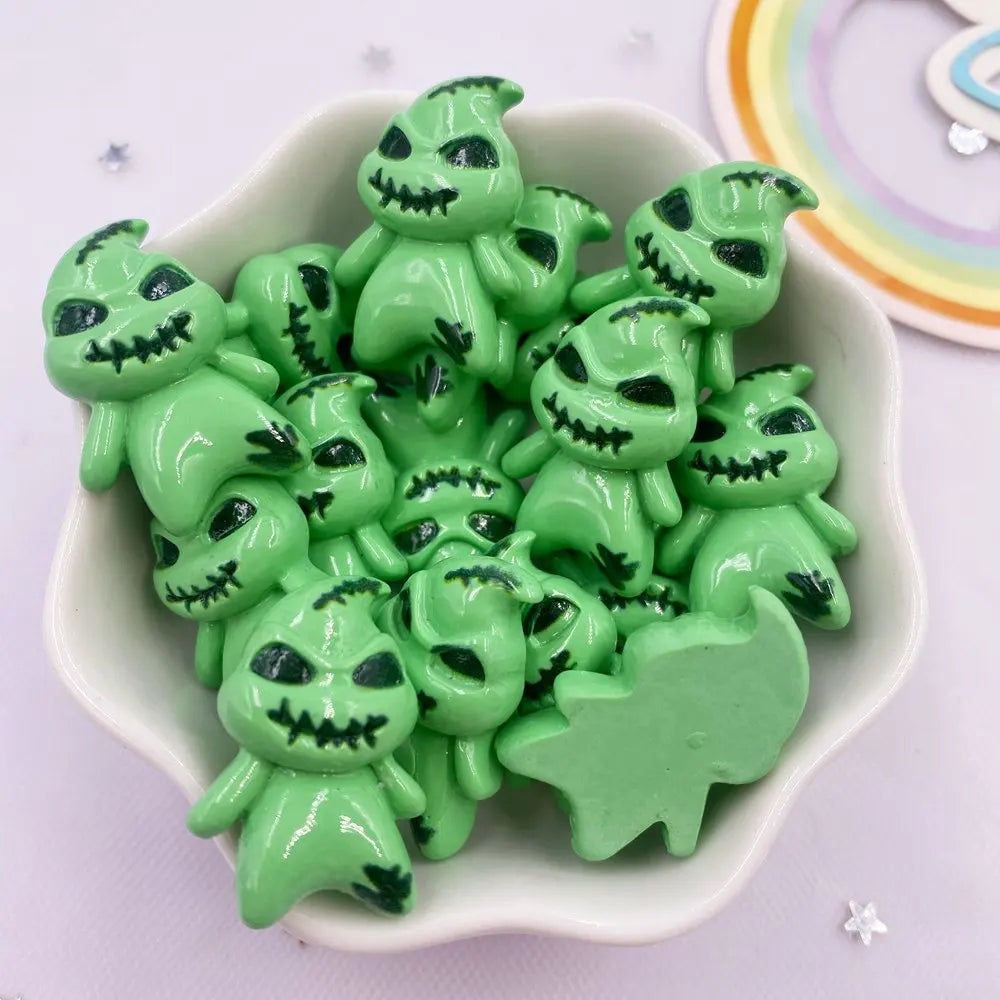 A collection of small, green resin flatback cabochon figurines with spooky faces in a white dish.
