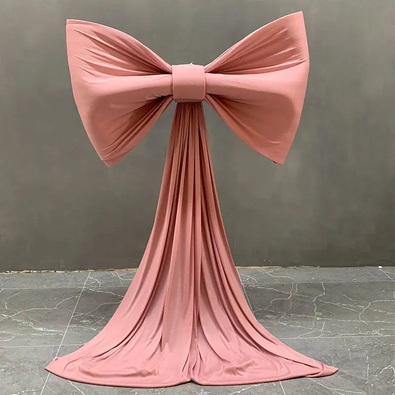 A large dusty rose satin bow with a long tulle drape used for event decoration.