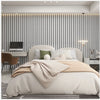 A bedroom featuring a bed with beige linens against a wall of vertical wooden slats and modern lighting.