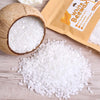 White beeswax pellets in a natural coconut shell and loose on a wooden surface.