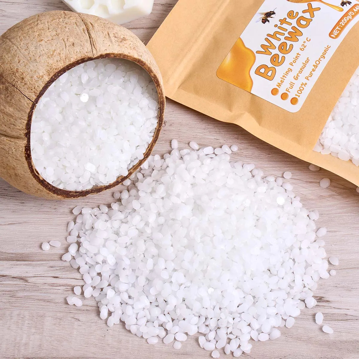 White beeswax pellets in a natural coconut shell and loose on a wooden surface.