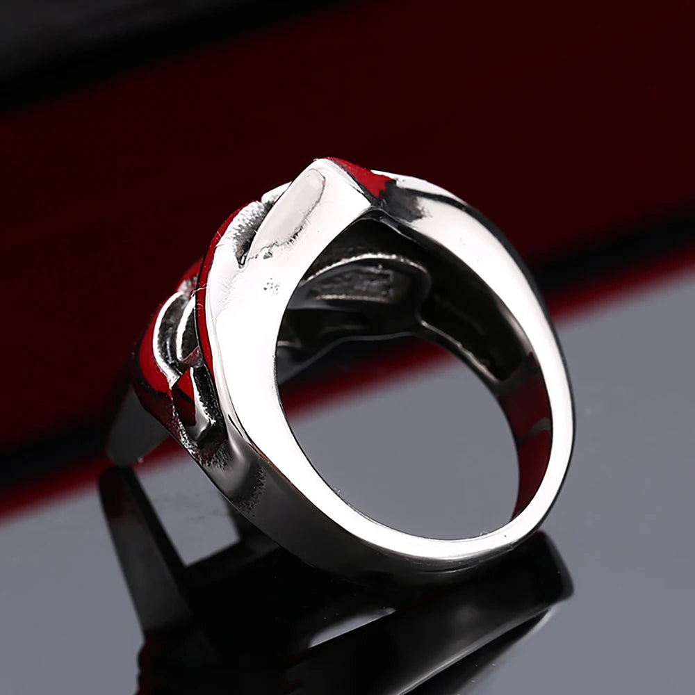 A silver stainless steel ring featuring a mask design with red accents, displayed on a dark reflective surface.