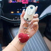 A hand holds a white electronic device keychain featuring a red heart charm on a wrist.