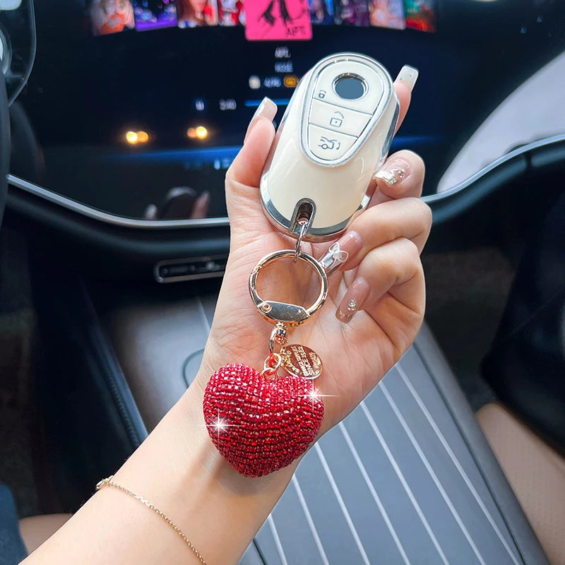 A hand holds a white electronic device keychain featuring a red heart charm on a wrist.
