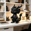 A black miniature dragon desk ornament stands on a white desk next to bookshelves.