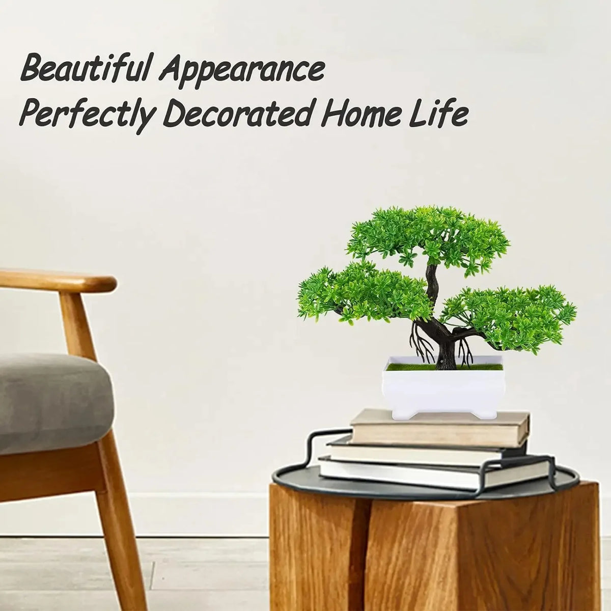 An artificial bonsai tree decoration in a white pot is displayed on a wooden table next to books.