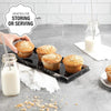 A clear acrylic cake stand with a lid displaying several muffins on a gray surface.