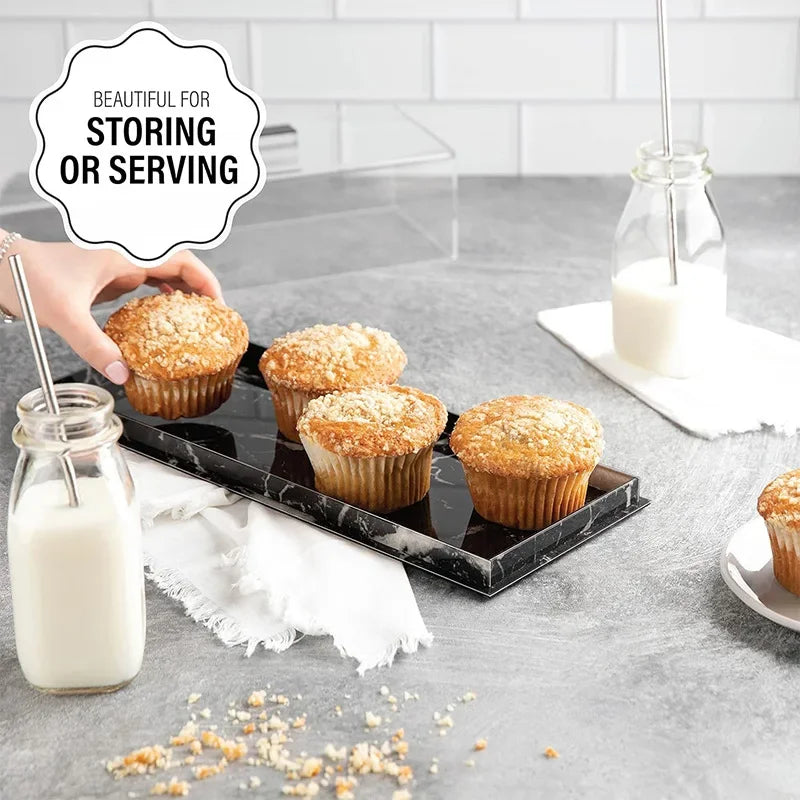 A clear acrylic cake stand with a lid displaying several muffins on a gray surface.