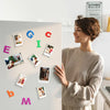 A woman displays a collection of colorful magnetic photo frames on a light gray wall.