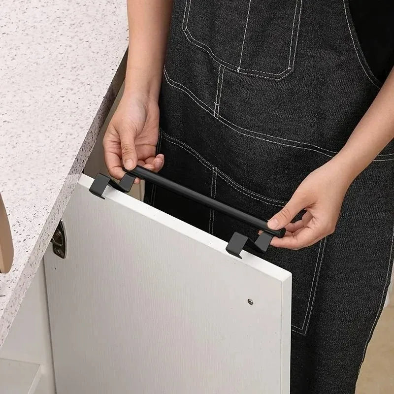 Une main installe un porte-serviette noir sur une porte de meuble blanc.