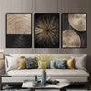 A set of three abstract canvas prints featuring concentric circle patterns in gold and black tones displayed on a modern sofa