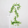 A white wooden stand displays a green artificial vine garland draped over two tiers.