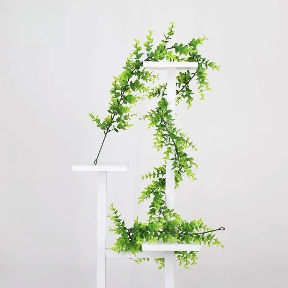 A white wooden stand displays a green artificial vine garland draped over two tiers.