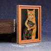 A framed picture of an orange tabby cat hugging a black cat, displayed in a wooden frame.