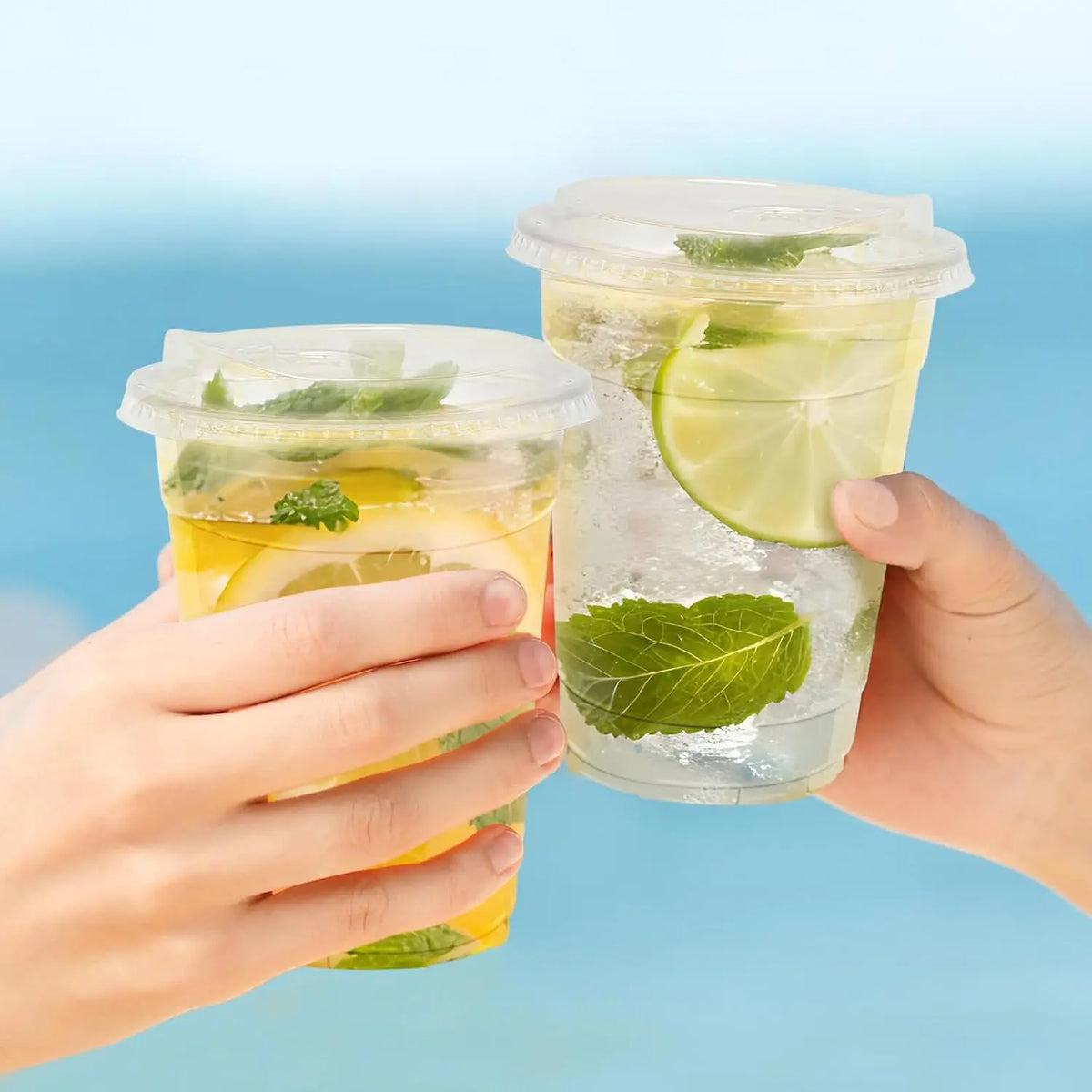 A hand holds a reusable clear plastic drinking cup filled with water and lime slices, featuring a flat lid.
