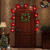 A wooden door decorated with red poinsettia garland lights and a green wreath on a textured wall.