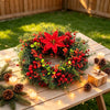 A festive wreath made of pine, eucalyptus, and red berries rests on a wooden table outdoors.