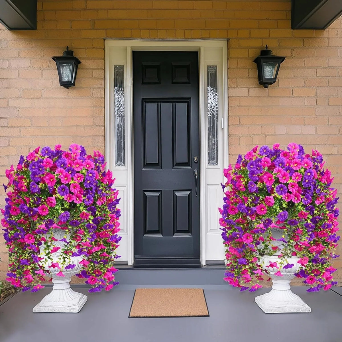 A pair of large white urns filled with vibrant purple and pink artificial flowers sit on a gray porch with a black door.
