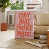A pink canvas art poster with the text PLAY THAT FUNKY MUSIC in orange lettering displayed indoors.