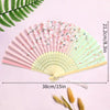 A pink and green elegant bamboo folding hand fan with a tassel displayed on a light purple background.