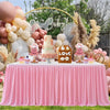A pink pleated polyester table skirt decorated with balloons, flowers, and a cake display for a celebration.