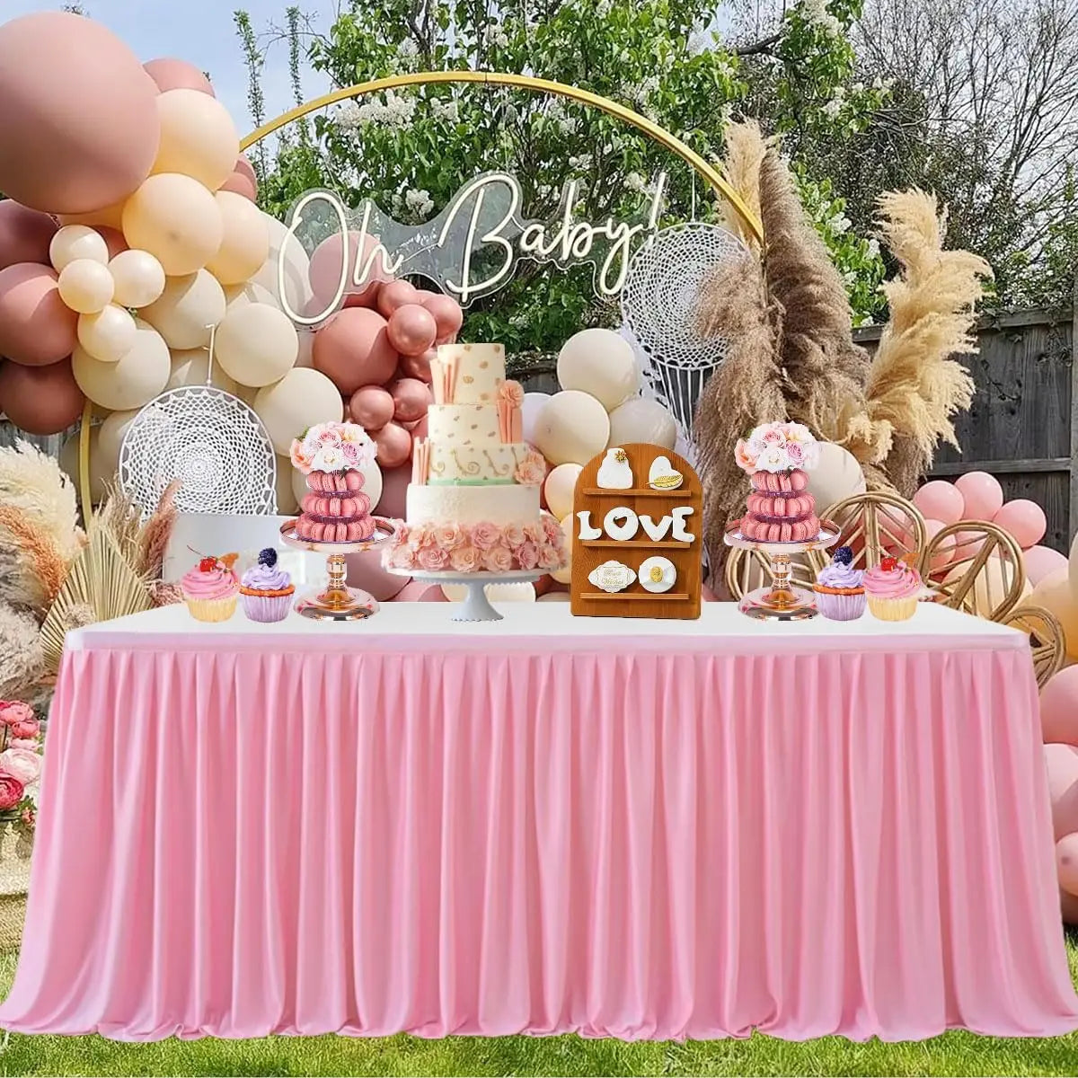 A pink pleated polyester table skirt decorated with balloons, flowers, and a cake display for a celebration.
