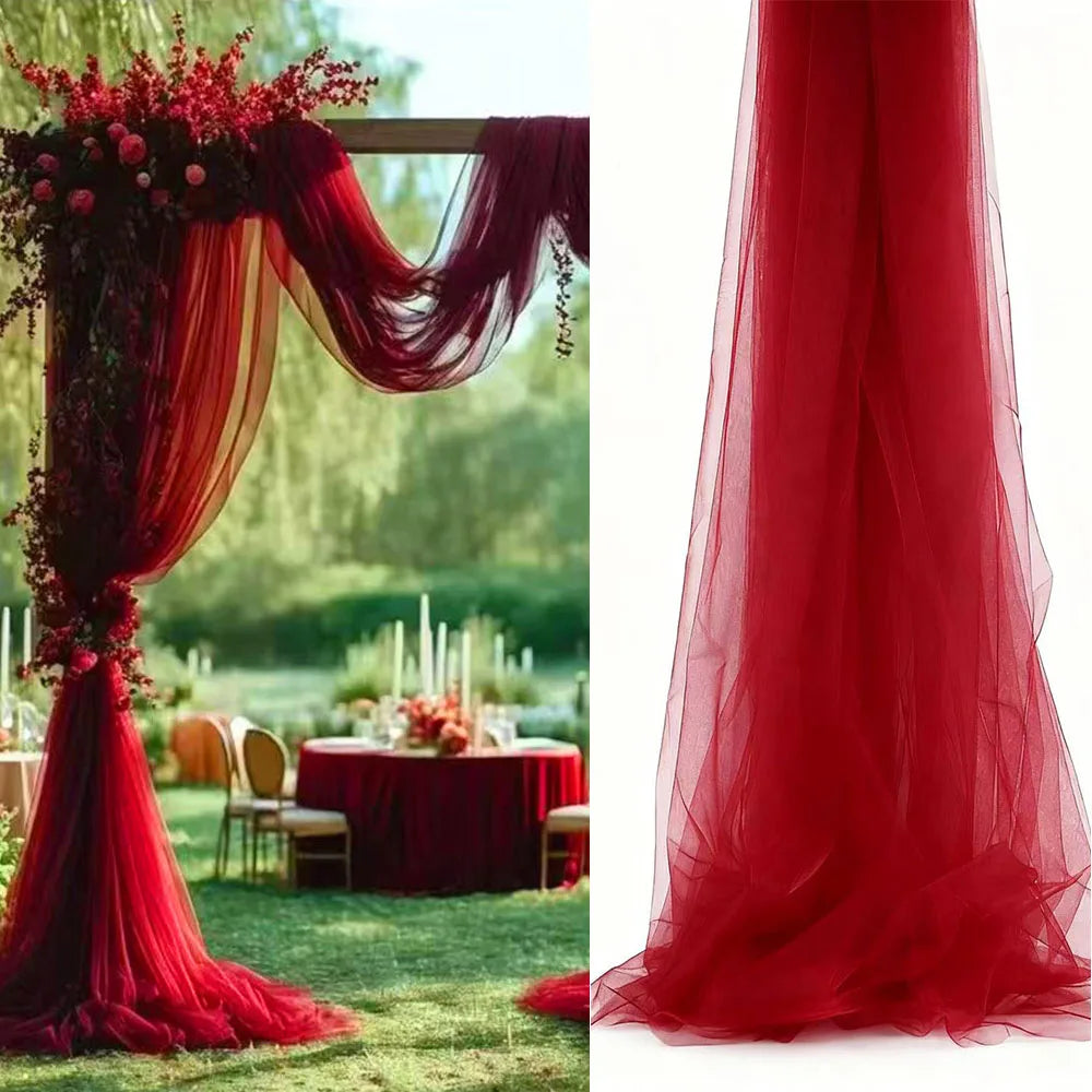 A flowing, sheer red tulle fabric draped vertically, used for a wedding arch backdrop.