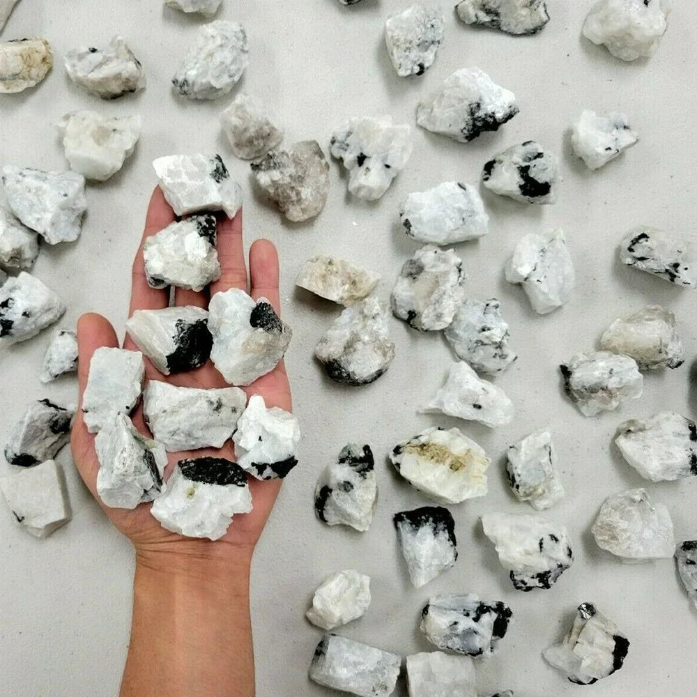 A hand holds numerous natural raw healing crystal stones scattered on a white surface.