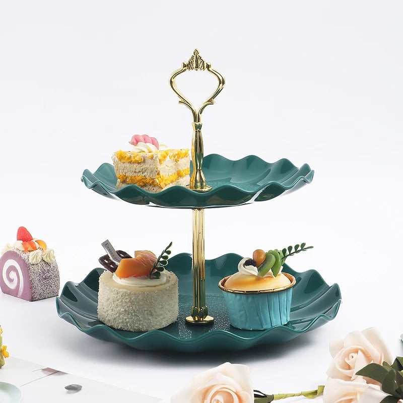 A gold two-tier serving stand holds a slice of cake and a small pastry on a green plate.
