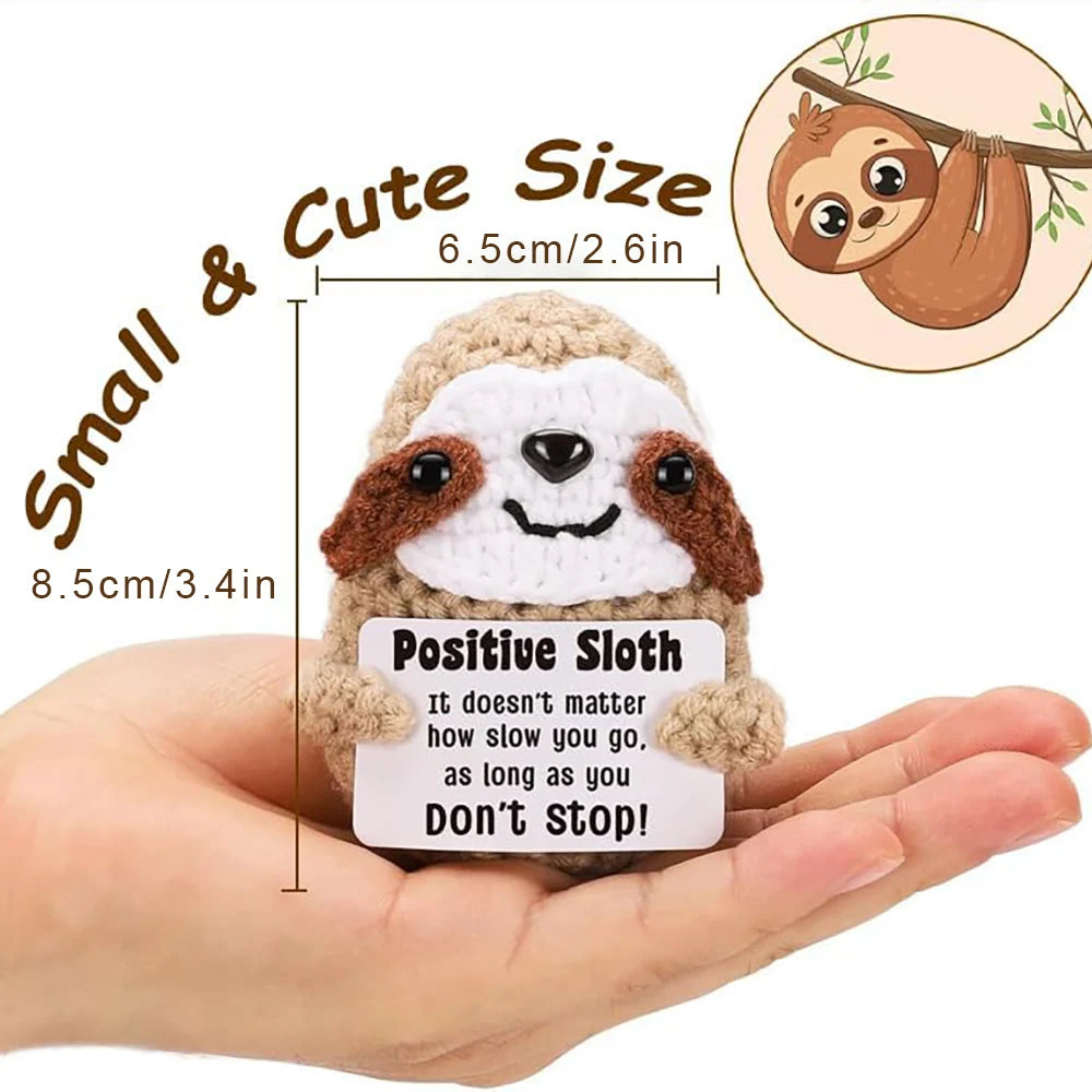 A handmade crochet sloth potato doll with a positive inspirational card held in a hand.