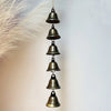 A vertical arrangement of small, antique bronze metal wind chimes hanging from a feather.