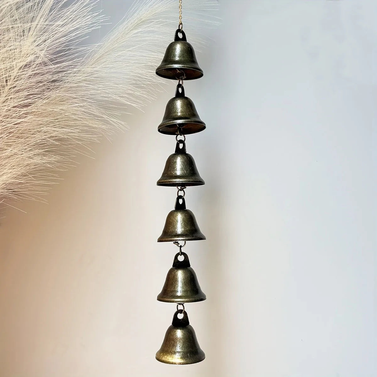 A vertical arrangement of small, antique bronze metal wind chimes hanging from a feather.