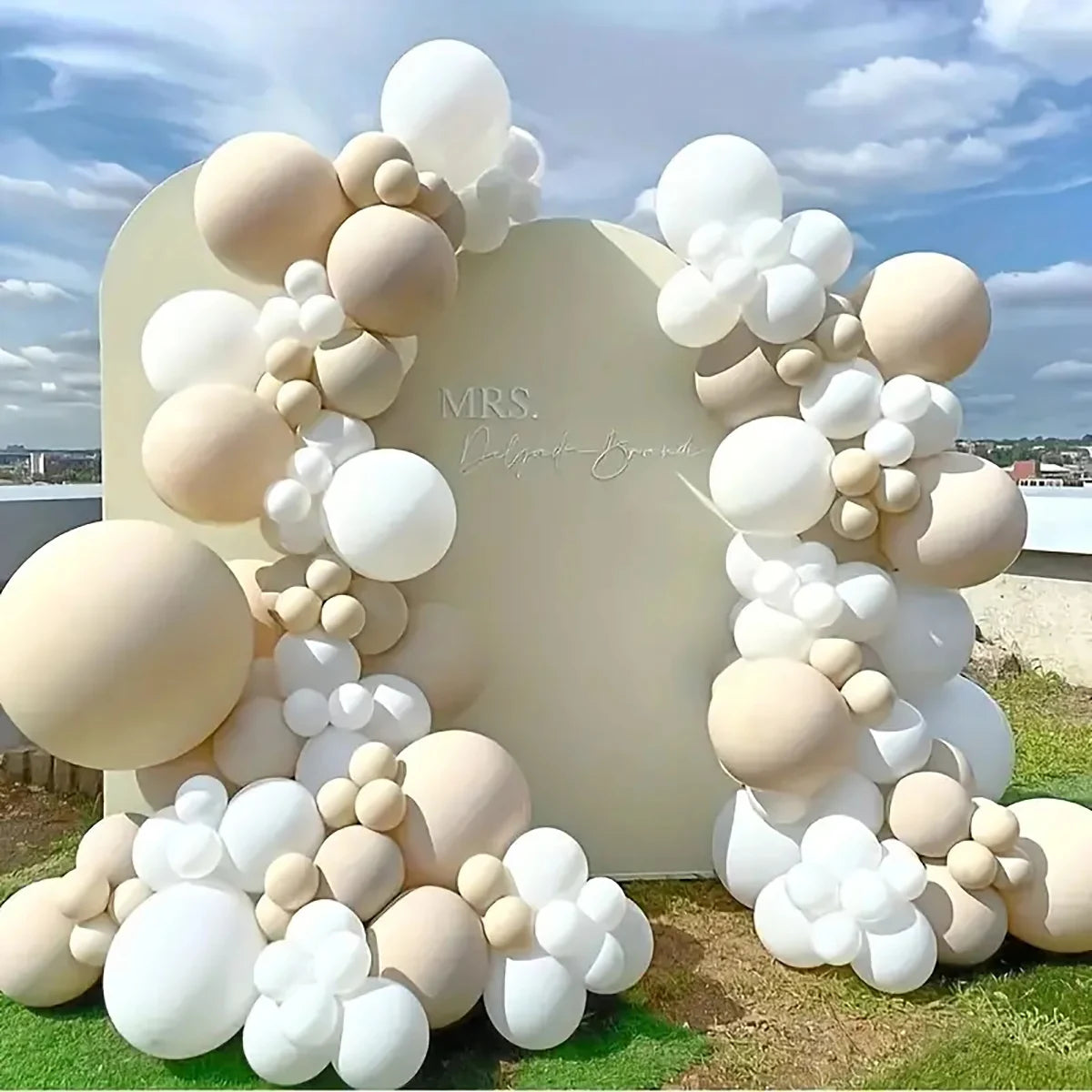A large balloon garland arch made of white and beige latex balloons set up for an event backdrop.