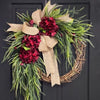 A rustic wreath made of green foliage and deep red berries tied with a natural burlap bow, suitable for door or wall decor.