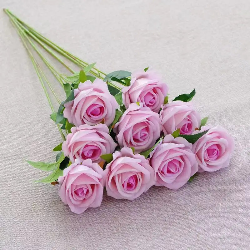 A bouquet of pink velvet artificial roses with green stems arranged on a light fabric.