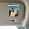A photo frame featuring a couple is clipped onto a car visor using a magnetic holder.