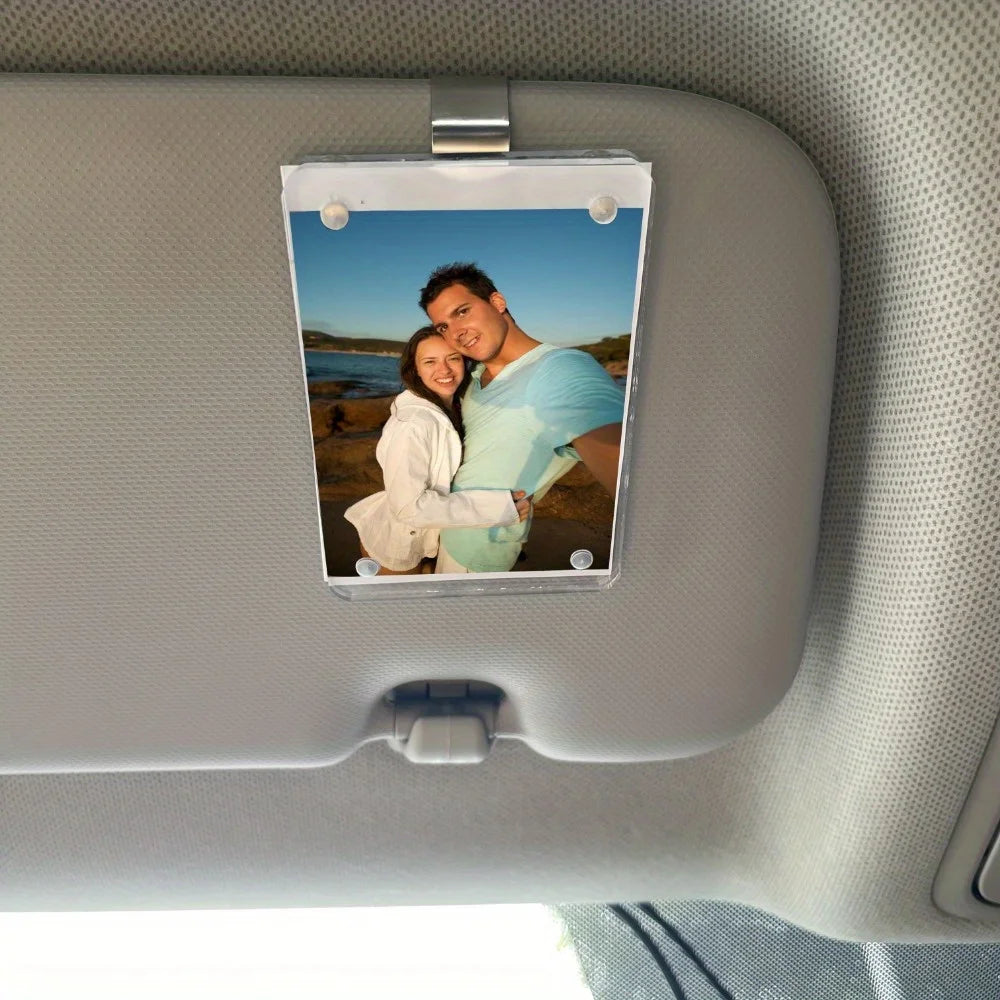 A photo frame featuring a couple is clipped onto a car visor using a magnetic holder.