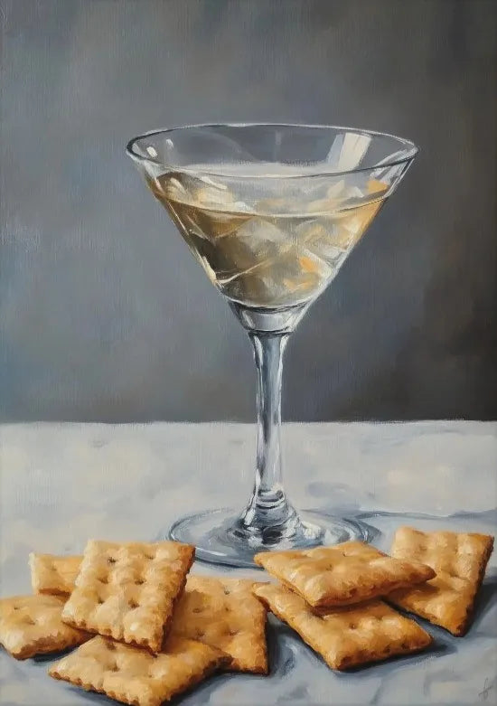 A glass of iced tea in a martini glass sits on a white surface with crackers nearby.