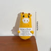 A yellow crochet giraffe doll with a white face and inspirational text on a tag.