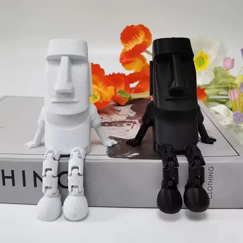 A white 3D printed Moai statue figurine with movable joints stands next to a black version on a box.