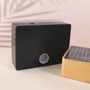 A black rectangular savings box with a circular opening is placed next to a light wooden piggy bank.