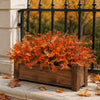 Eine Pflanze gefüllt mit künstlichen Herbstblumen in leuchtendem Orange und Rot, vor einem dunklen Metallgeländer.