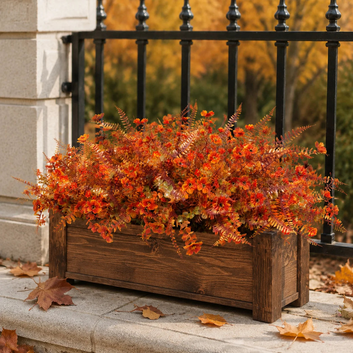 Eine Pflanze gefüllt mit künstlichen Herbstblumen in leuchtendem Orange und Rot, vor einem dunklen Metallgeländer.