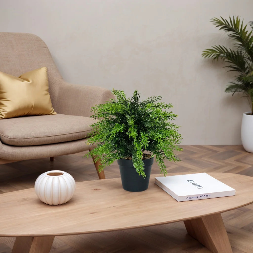 A potted artificial cypress topiary with bright green foliage sits on a wooden table next to a white ceramic sphere.
