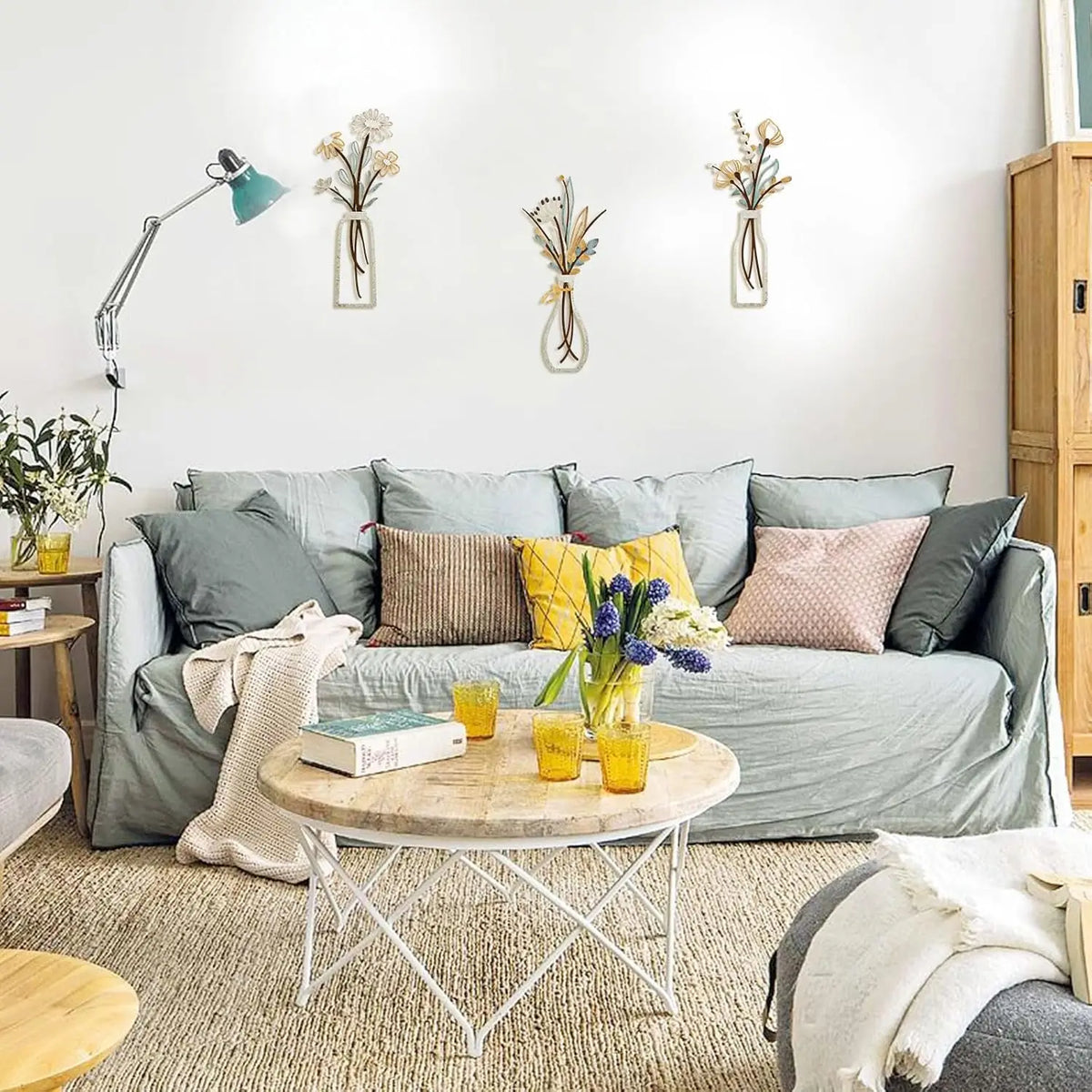 A living room wall decorated with three metal vases holding dried flowers and a light blue lamp.