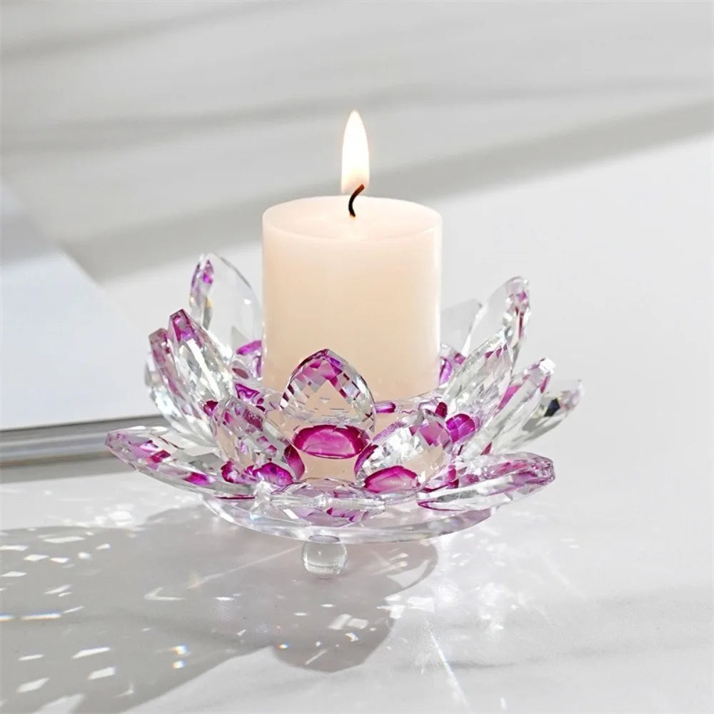 A clear crystal lotus candle holder with a white pillar candle and flame on a white surface.