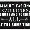 A black rectangular metal sign with white text that reads I'M MULTITASKING I CAN LISTEN IGNORE AND FORGET ALL AT THE SAME TIM