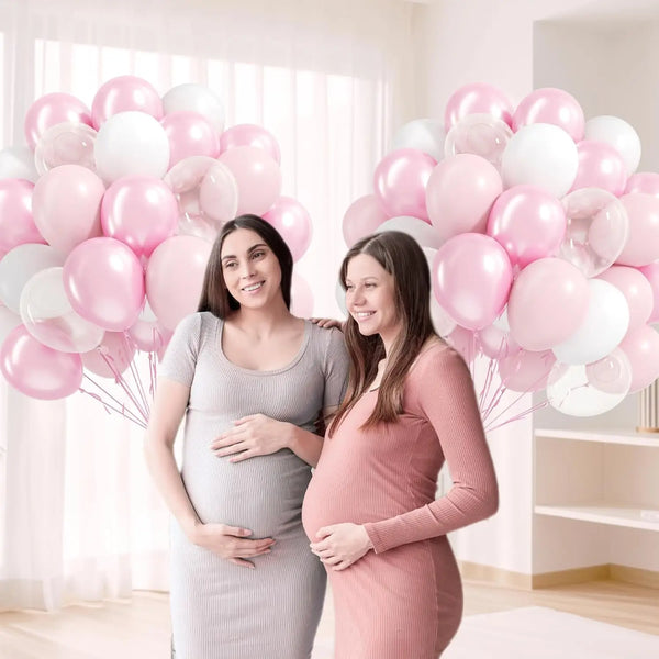 Two women in maternity dresses stand holding a large pink and white balloon bouquet.
